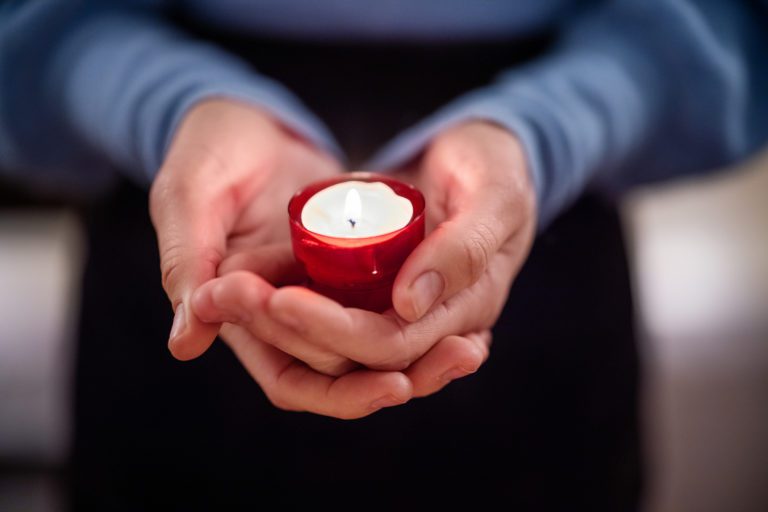 Close-up of person in blue sweatshirt holding a candle in red holder