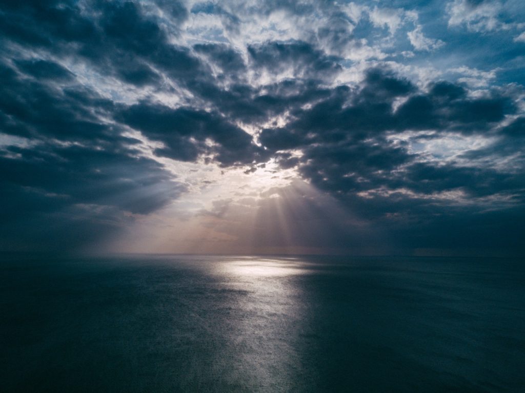 An ocean with darkish blue clouds and a light of ray reflecting